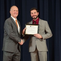 Doctor Potteiger posing for a photo with an award recipient in a light grey suit and a red shirt